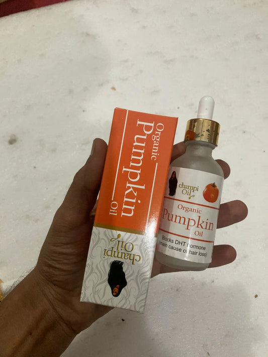 Hand holding a bottle and orange box of Champi Oil Organic Pumpkin Oil for hair loss