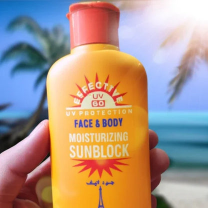 Hand holding yellow bottle of Effective UV 60 Face & Body Moisturizing Sunblock with beach background