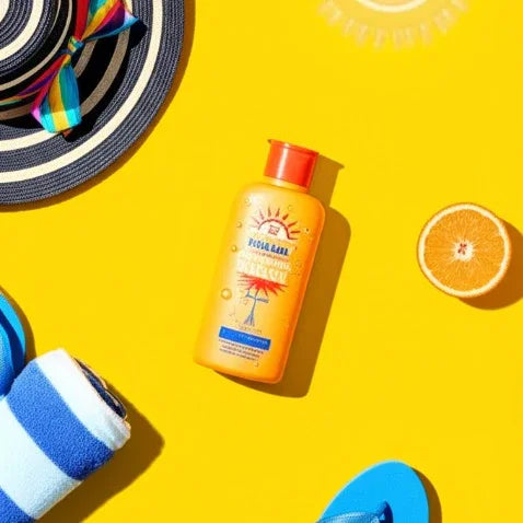 Sunscreen bottle with SPF label, colorful hat, blue flip-flop, and orange on a yellow background